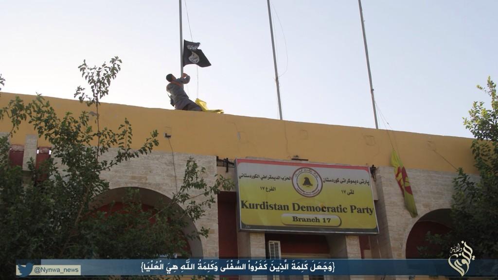 Militant hoisting the Islamic State flag, replacing the Kurdish flag 