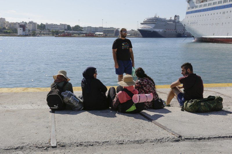 A family of refugees sits on the ground in Piraeus Harbour, watching out towards the sea, waiting for the bus to bring them to the metro station. Photo by Michael Debets Copyright Demotix (28/9/2015). 