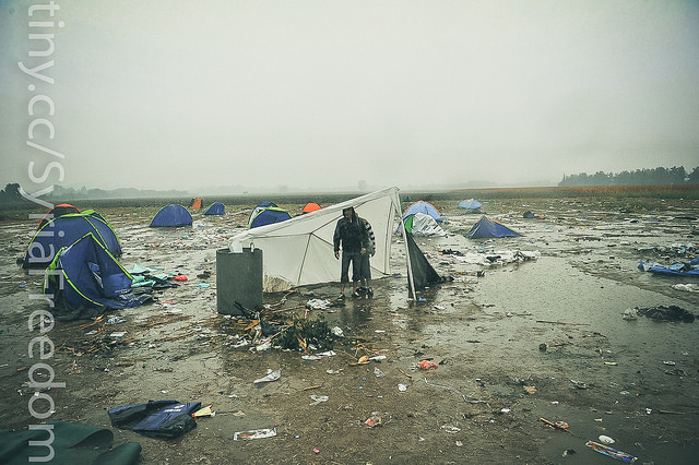 Emigrantes y refugiados intentan protegerse de la lluvia mientras esperan para cruzar la frontera entre Grecia y Macedonia en Idomeni, 10 de Septiembre de 2015. Foto de Freedom House en Flickr, de dominio público