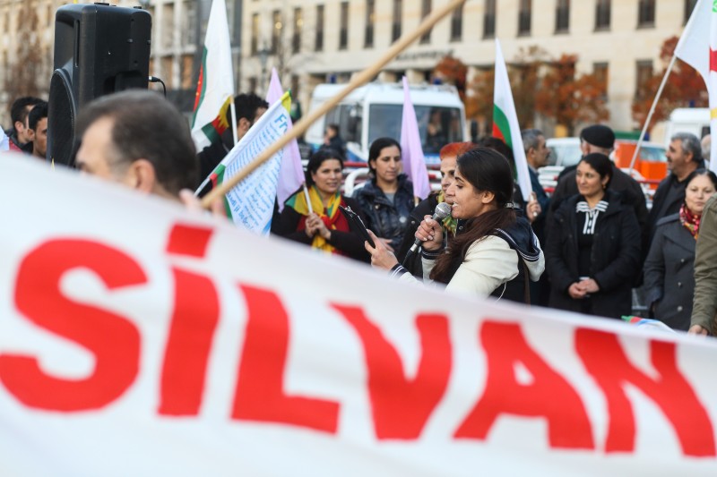 Berlin, Germany. 12th November 2015 -- A woman gives a speech behind a banner remembering Silvan. -- Dozens Kurds and Yazidi rally at Berlin's Brandenburg Gate to condemn Turkish attacks on and the siege of Kurdish Silvan in Turkey. They also remember the fate of the Yazidi in Iraq who are murdered and enslaved by the Islamic State (ISIS) .