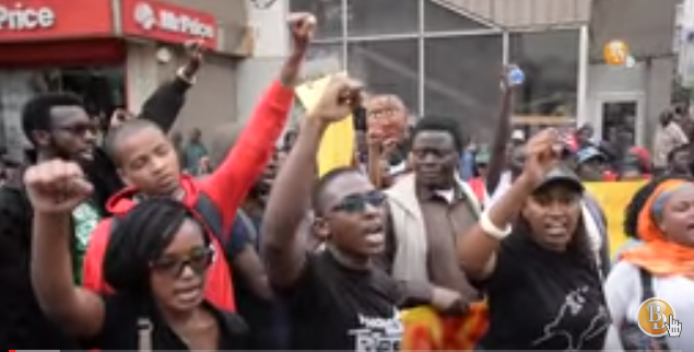 A screenshot of a YouTube video of Kenyans taking part in #TakeBackKenya protest in Nairobi singing with raised fists. 