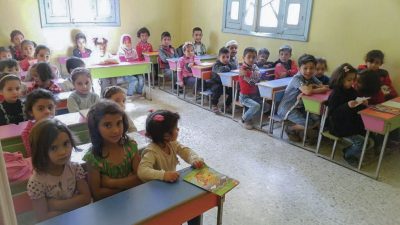 Children in a classroom in Raqqa, Syria, sitting at desks and looking at the photographer.