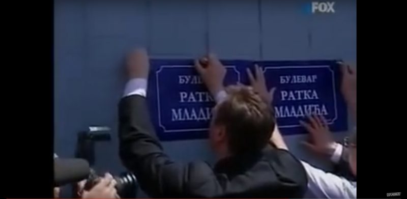 Capture d'écran d'un reportage sur un événement de 2007 en soutien à Ratko Mladić, impliquant le président serbe actuel Aleksandar Vučić, 10 ans avant son entrée en fonction. Sur la photo, il colle une affiche sur le boulevard Ratko Mladić.