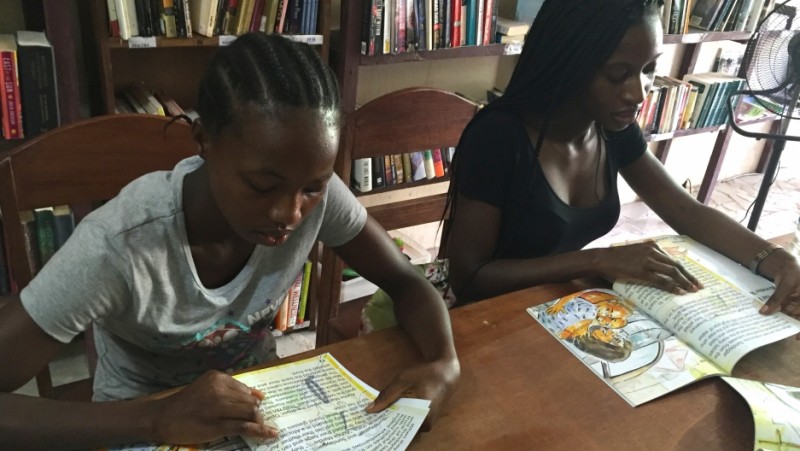 Girls like Miatta (left) come to storytime at One Moore Bookstore in Monrovia. Owner Wayétu Moore (right) also publishes books like the one they're reading, "Gbagba," a Liberian word that means "corruption." Credit: Prue Clarke. Used with PRI's permission