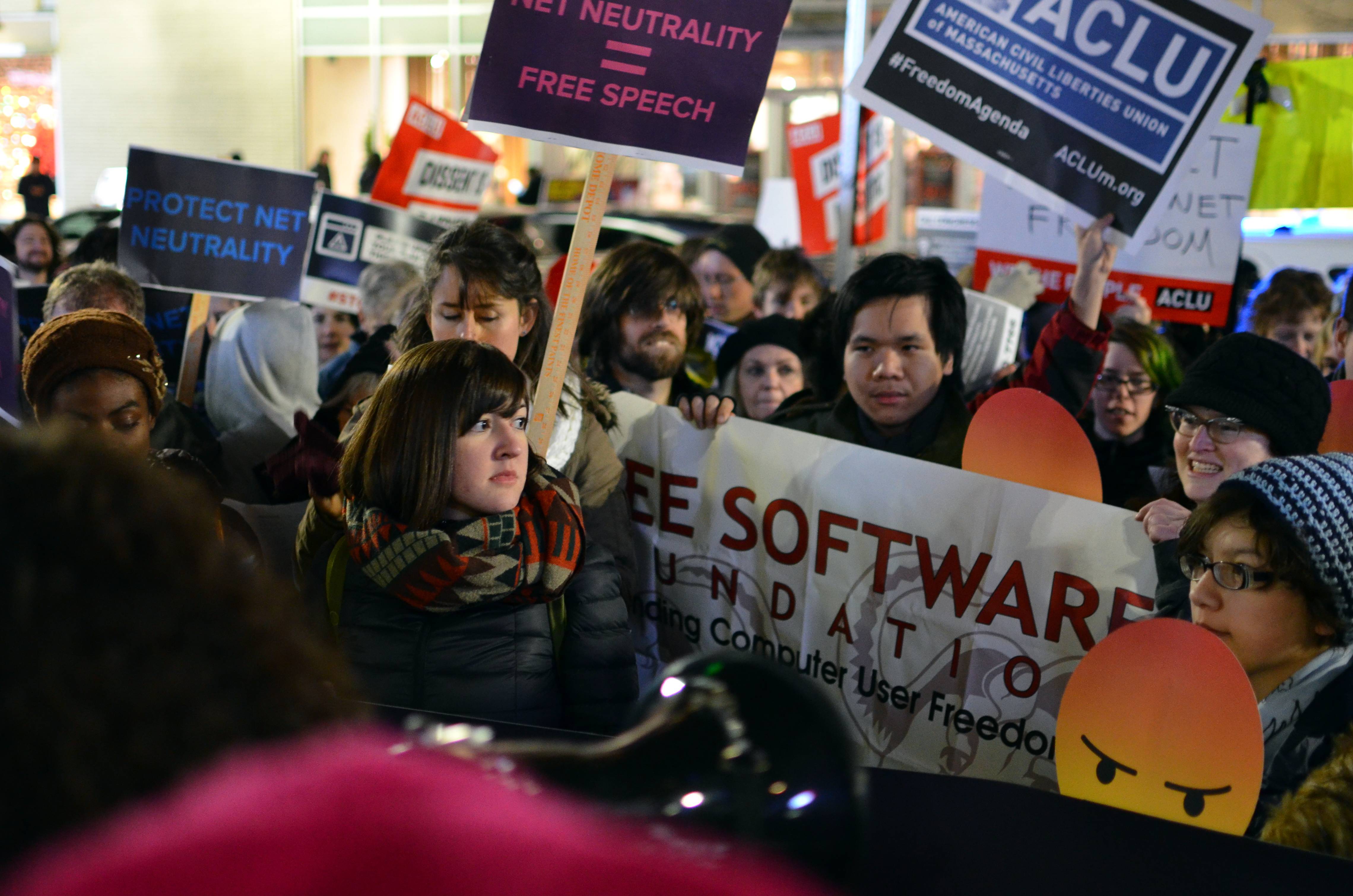 A photo of a protest, with people wearing scarves and hats and signs, including a banner that says 