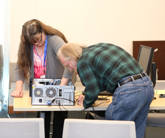 a man and woman tinkering with a desktop computer.